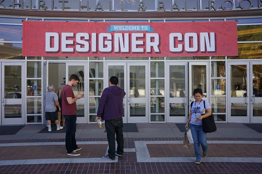 Red banner with white text reading ’DESIGNER CON’ mounted above glass entrance doors.